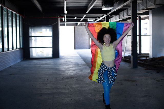 African american transgender woman holding lgbt flag in empty parking garage. concept of gender expression, identity and diversity.