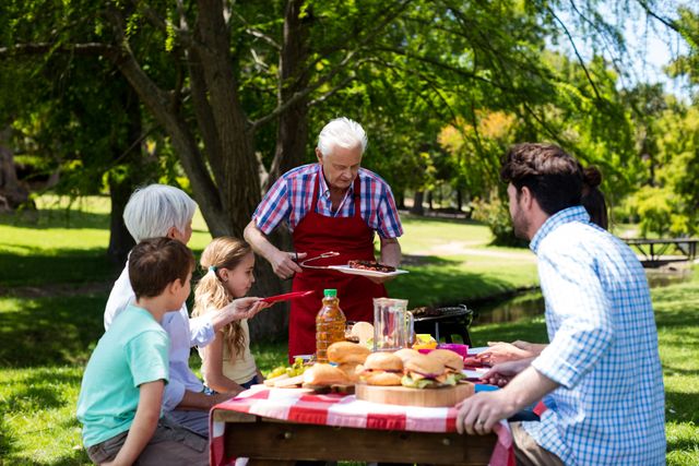 Senior man serving barbeque to family in park on a sunny day