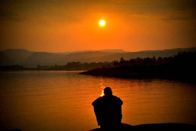 Silhouette of Person Sitting Beside Body of Water at sunset - Download Free Stock Photos Pikwizard.com