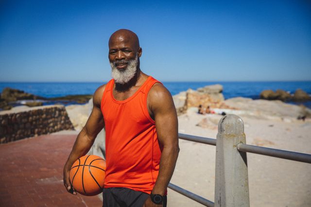 Portrait of african american senior man holding basketball while standing on the promenade. retirement sports and active senior lifestyle.