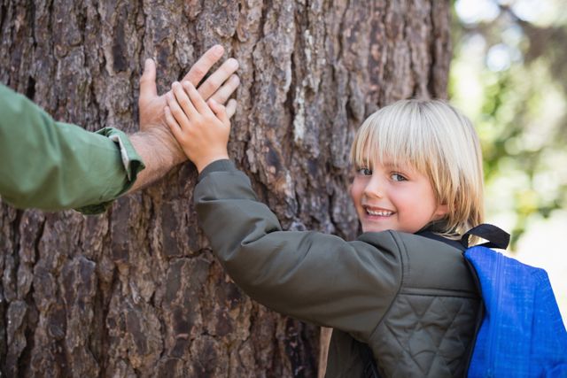 Smiling son with father father touching tree trunk in forest - Download Free Stock Photos Pikwizard.com