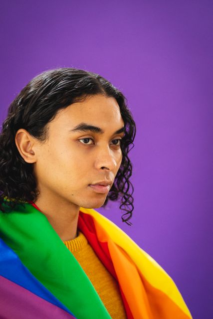 Close-up of biracial thoughtful young man with rainbow flag looking away against purple background - Download Free Stock Photos Pikwizard.com
